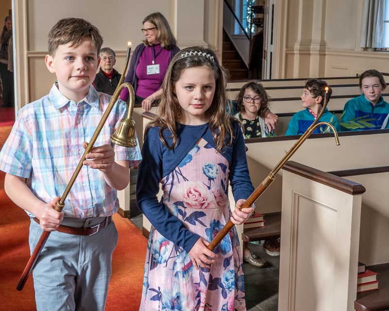 Two young acolytes walk with lit tapers to light the alter candles at the start of a worship service