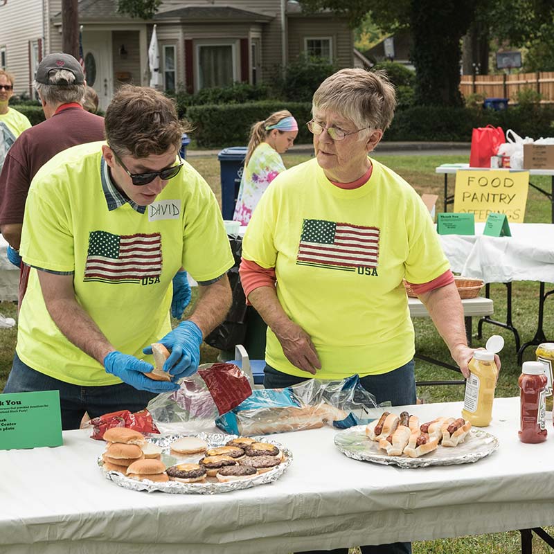 Two volunteers set out grilled food at neighborhood block party sponsored by East Church