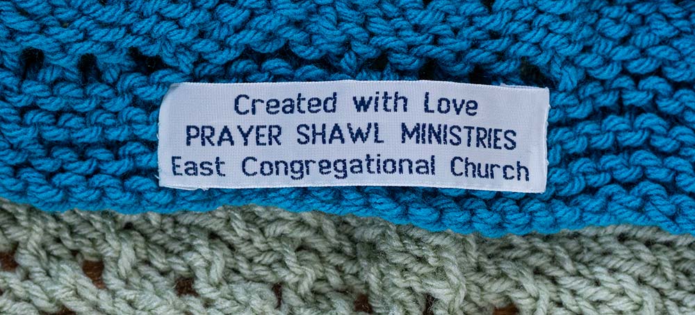 Tag affixed to knitted shawl stating "Created with Love Prayer Shawl Ministries East Congregational Church"