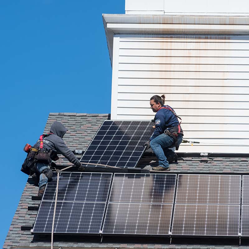 technicians install solar panels on East Church roof